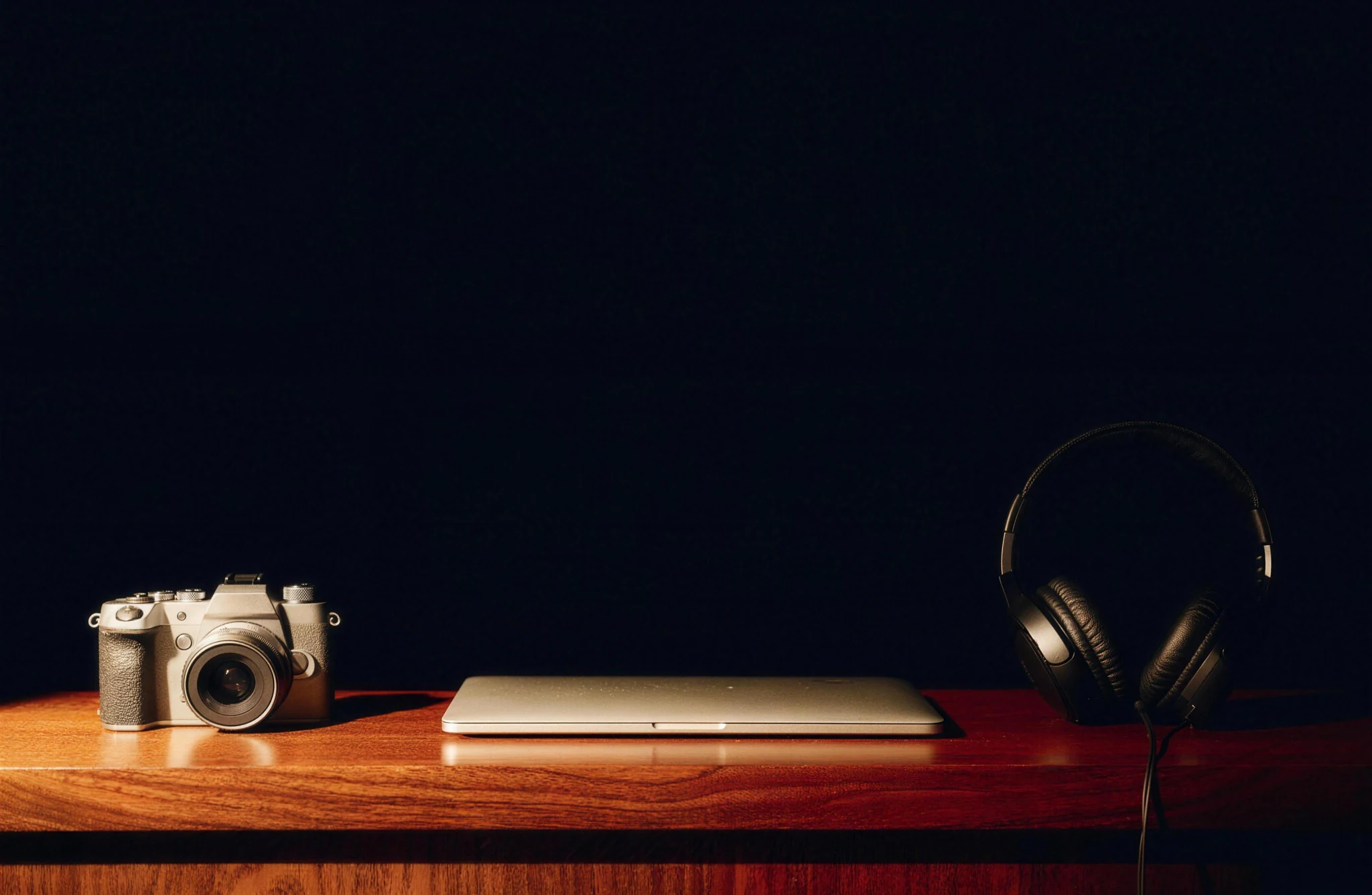 Camera, laptop and over-ear headphones on a timber counter